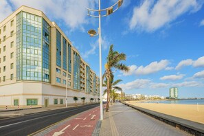 Un hôtel situé en bord de mer, doté d’une façade incurvée, d’une piste cyclable et d’une promenade bordée de palmiers.