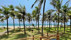 A beach view with palm trees, a heart-shaped sculpture, and a wooden fence. - Wai Wai Cumbuco Resort (Caucaia)