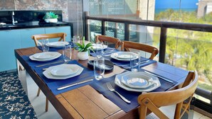 A dining table set with plates, glasses, and cutlery, with a view of the sea through large windows. - Wai Wai Cumbuco Resort (Caucaia)