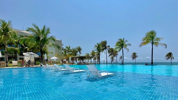 A pool area with lounge chairs and umbrellas, surrounded by palm trees and a clear view of the ocean. - Wai Wai Cumbuco Resort (Caucaia)