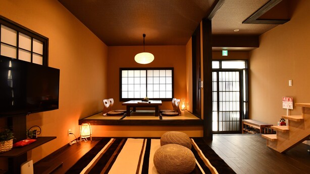 Una camera in stile tradizionale giapponese con pavimento in tatami, un tavolino con cuscini, una televisione e una porta scorrevole.