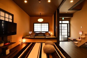 Une pièce de style japonais traditionnel, avec un sol recouvert de tatamis, une petite table basse avec des coussins, un téléviseur et une porte coulissante.