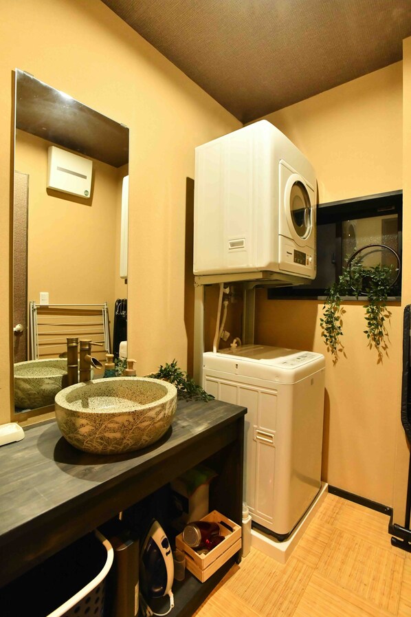 Une petite salle de bain dotée d’un grand lavabo rond en pierre, d’un lave-linge blanc et d’un miroir placé au-dessus du lavabo.