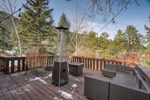 A wooden deck with outdoor furniture, a tall metal heater, and a view of trees and a cabin. - Moose Manor  (Cascade)