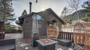 En træhytte med en terrasse, udendørs siddepladser og et bålsted.