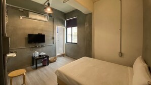 Un dormitorio con una cama grande, un televisor en la pared, una mesita con objetos y una ventana con vistas.