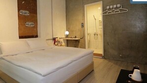 Un dormitorio con cama, mesita de noche, estante en la pared con lámpara, perchero y zona de ducha.