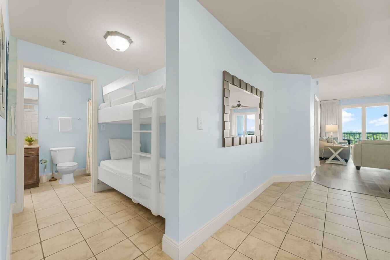 Een kamer met stapelbedden, een badkamer met toilet en wastafel, en een zithoek met een bank en balkon.
