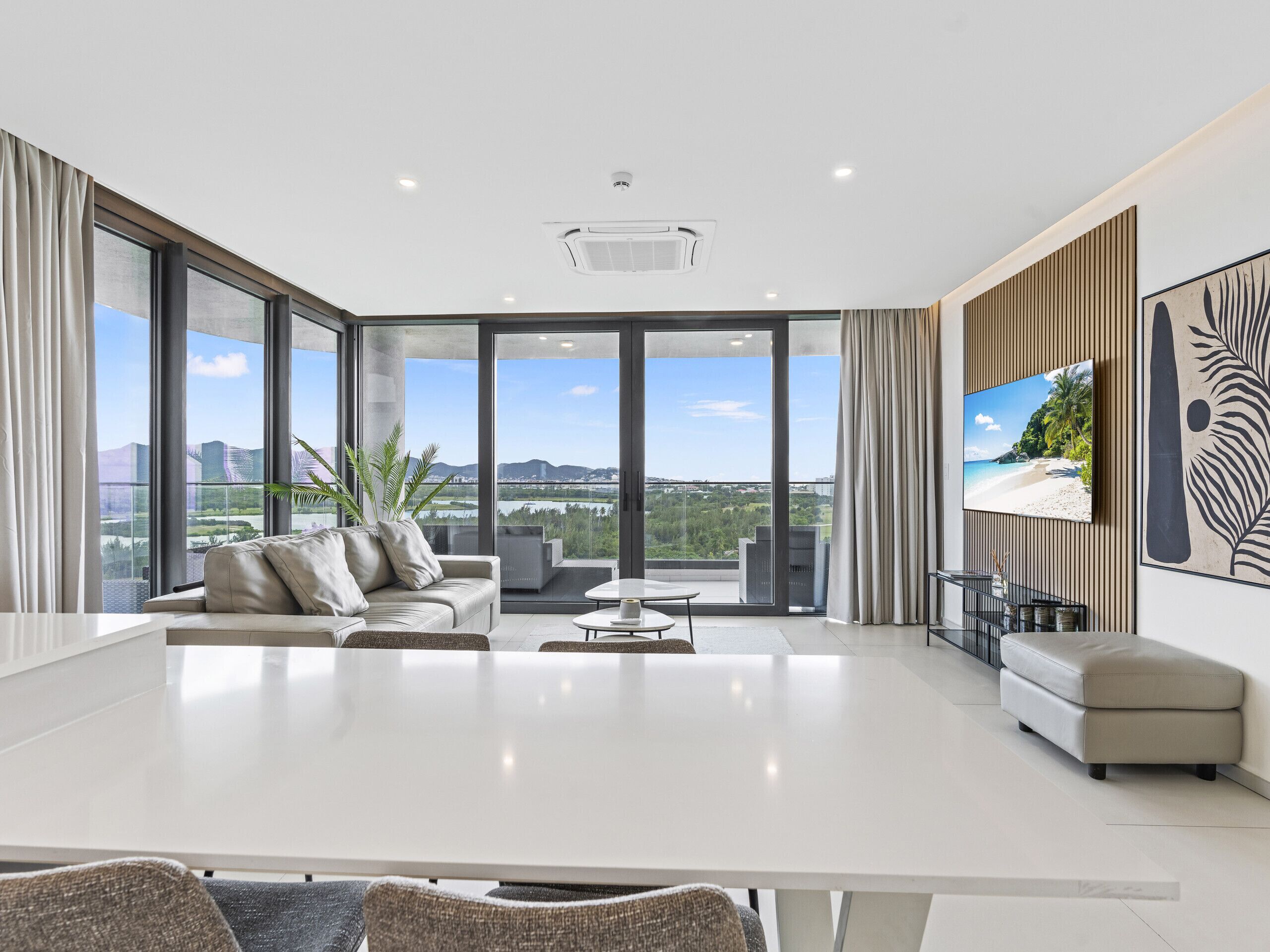 A modern living room with a large white table, a sofa, and a TV on the wall.