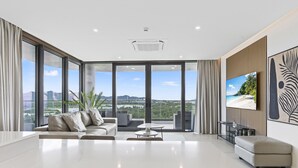 A modern living room with a large white table, a sofa, and a TV on the wall. - B-1004 Stunning corner apartment with spectacular views (Cupecoy)