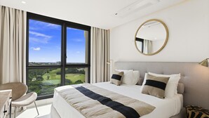 A modern hotel room with a large bed, a round mirror, a desk, and a view of a golf course. - B-1004 Stunning corner apartment with spectacular views (Cupecoy)