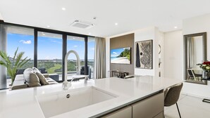 A modern kitchen with a large island, a dining area with a view, and a living space with a large window overlooking a beach. - B-1004 Stunning corner apartment with spectacular views (Cupecoy)