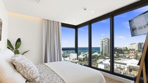 A bedroom with a large window, a bed, a plant, and a TV. - B-901 Corner apartment with stunning beach view (Cupecoy)