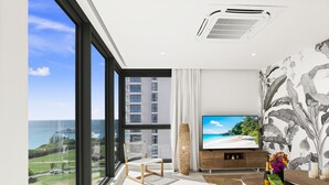 A modern living room with a large TV, a view of the ocean, and a tropical wallpaper. - B-901 Corner apartment with stunning beach view (Cupecoy)