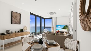 A dining area with a view of the sea, a wooden dining table, white chairs, and a modern kitchen with a wooden cabinet. - B-901 Corner apartment with stunning beach view (Cupecoy)