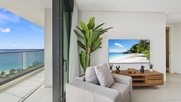Ein modernes Wohnzimmer mit großem Fernseher, einem grauen Sofa, einem Holztisch und einer großen Pflanze.