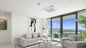 Ein modernes Wohnzimmer mit grauem Sofa, einem Couchtisch und Blick auf eine Stadtlandschaft durch große Fenster.