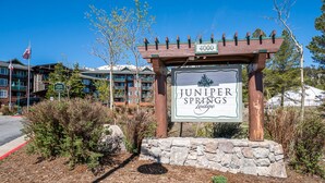 Juniper Springs Lodge -hotellin kyltti, jossa on kivijalusta ja puinen kaari, ja sen ympärillä on hoidettuja pensaita ja taivaalla ei ole pilviä.