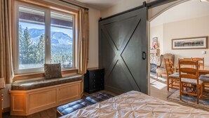 Makuuhuoneessa on suuri sänky, ikkunan vieressä penkki, ruokailutila, jossa on pöytä ja tuolit, sekä liukuovi, joka johtaa toiseen huoneeseen.
