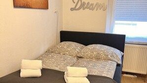 Uma cama bem arrumada com cabeceira escura, um mapa-múndi na parede e uma placa com a inscrição 'Relax Dream'.