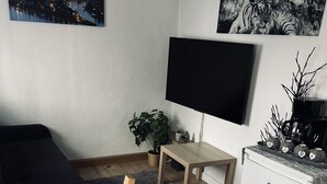 Um espaço de estar moderno e compacto, com cama, escrivaninha, televisão e uma pequena cozinha.