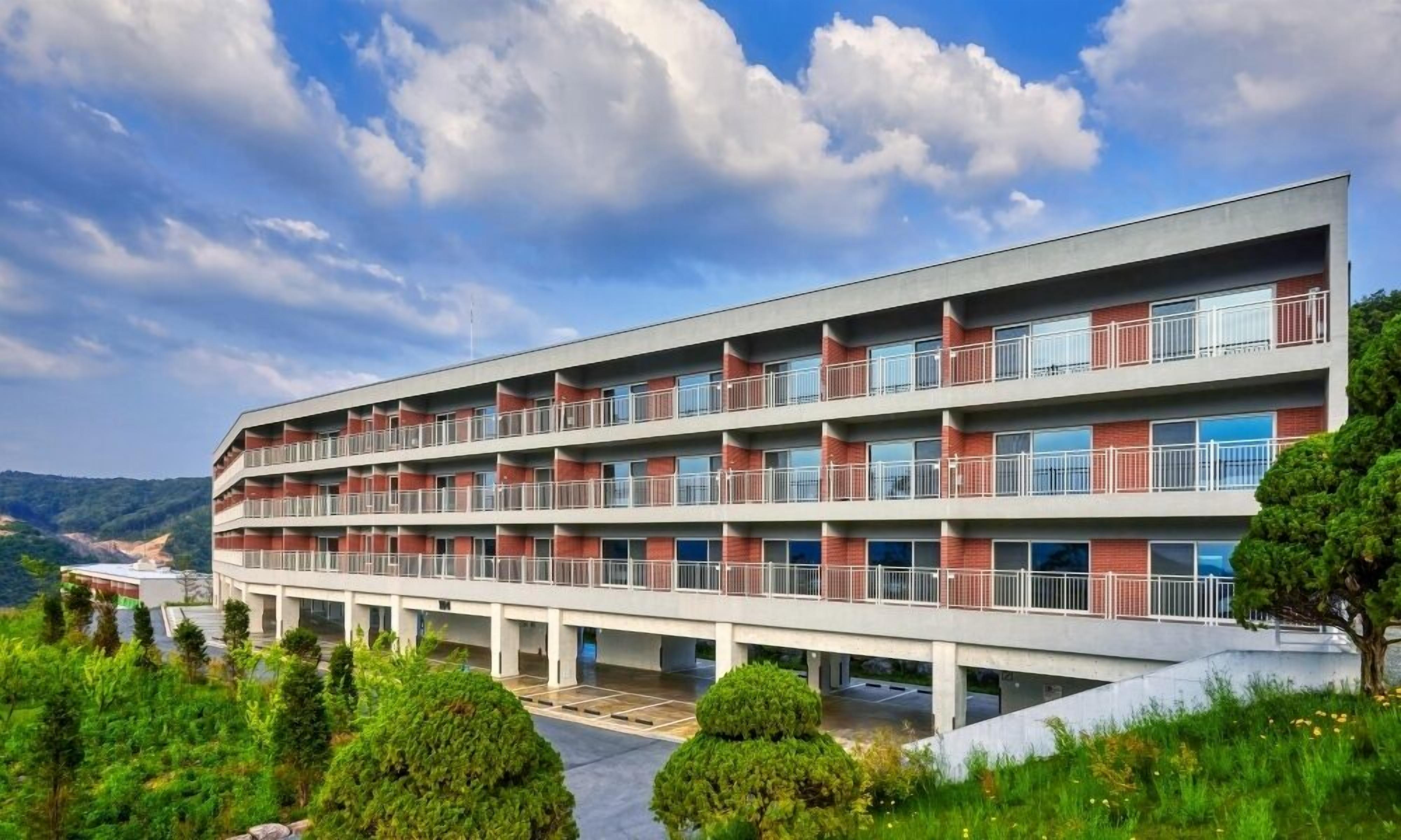 A multi-story hotel with balconies, a flat roof, and a parking area.