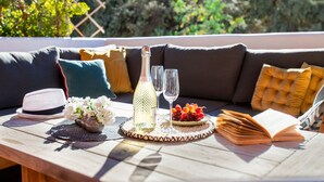 Une table en bois avec une bouteille, des verres, un bol de fruits, un livre et un chapeau.