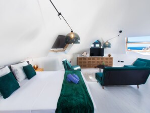Een moderne slaapkamer met een bed, een bank, een televisie en uitzicht op zee.
