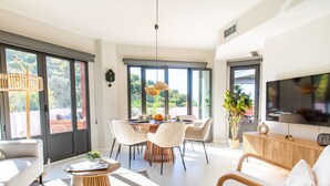 Un salon moderne comprenant un coin repas, de grandes fenêtres et un téléviseur à écran plat.