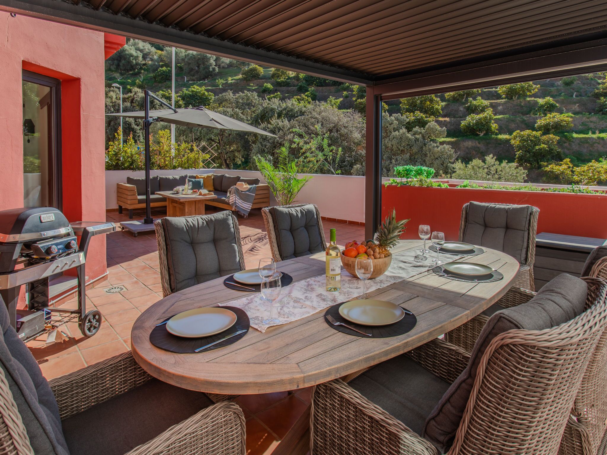 Un espacio para comer al aire libre con una mesa redonda, sillas de mimbre y una parrilla.