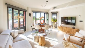 Un salon moderne avec un grand canapé, un coin repas avec des chaises, un téléviseur et une grande fenêtre donnant sur un paysage verdoyant.