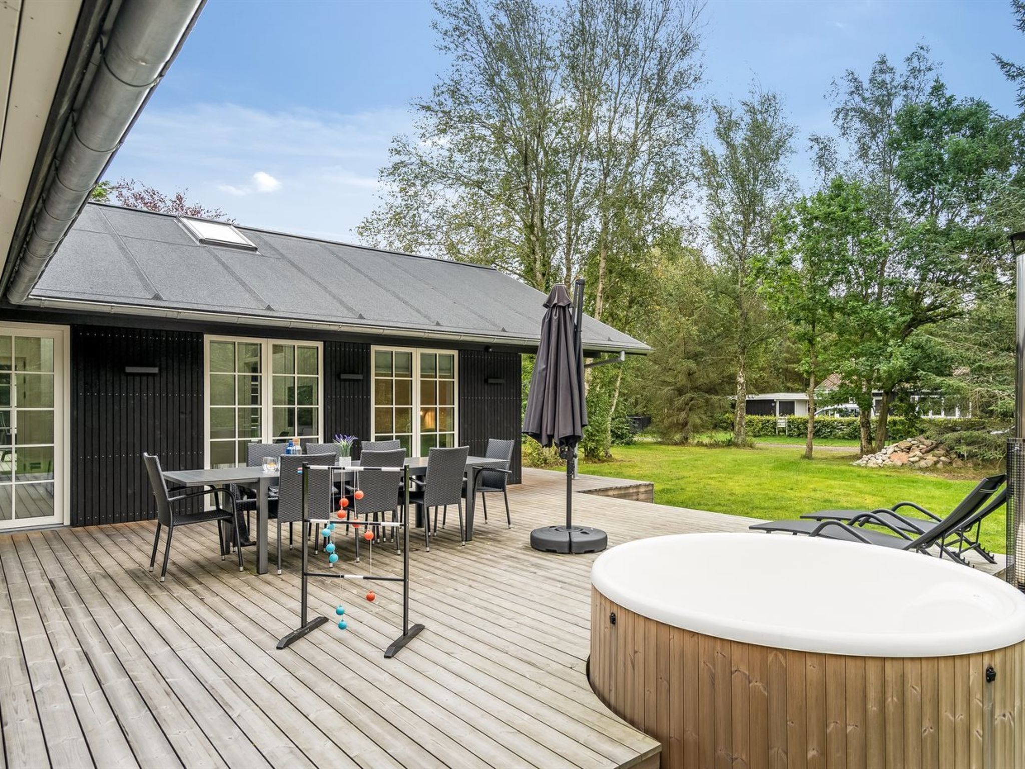 Une terrasse en bois avec un jacuzzi, un coin salon extérieur et un espace repas comprenant une table et des chaises.