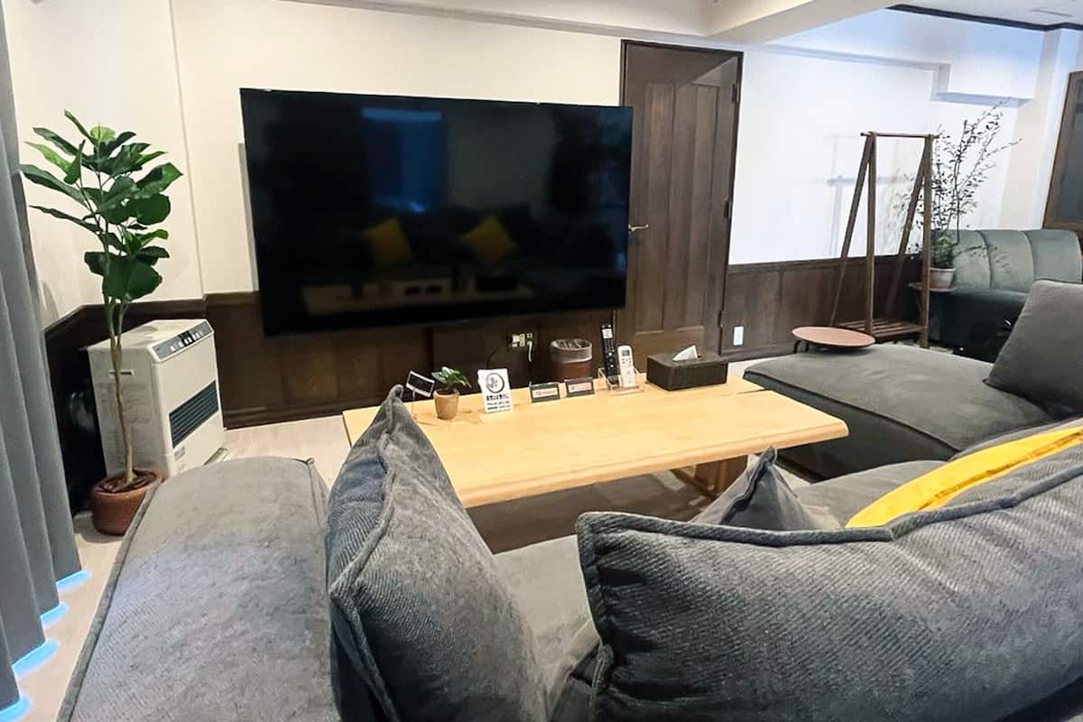 A modern living room with a flat-screen TV, grey sofas, a wooden coffee table, and a potted plant.