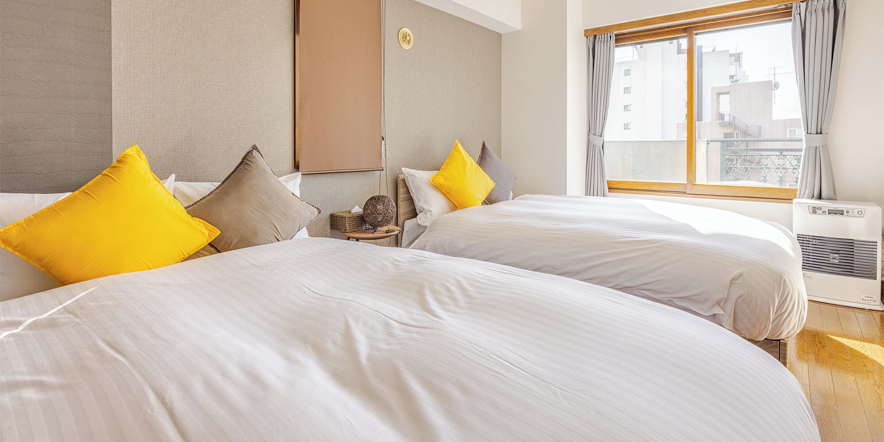 A hotel room with two beds, a window with curtains, and an air conditioning unit.