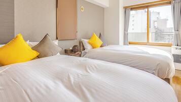 A hotel room with two beds, a window with curtains, and an air conditioning unit.