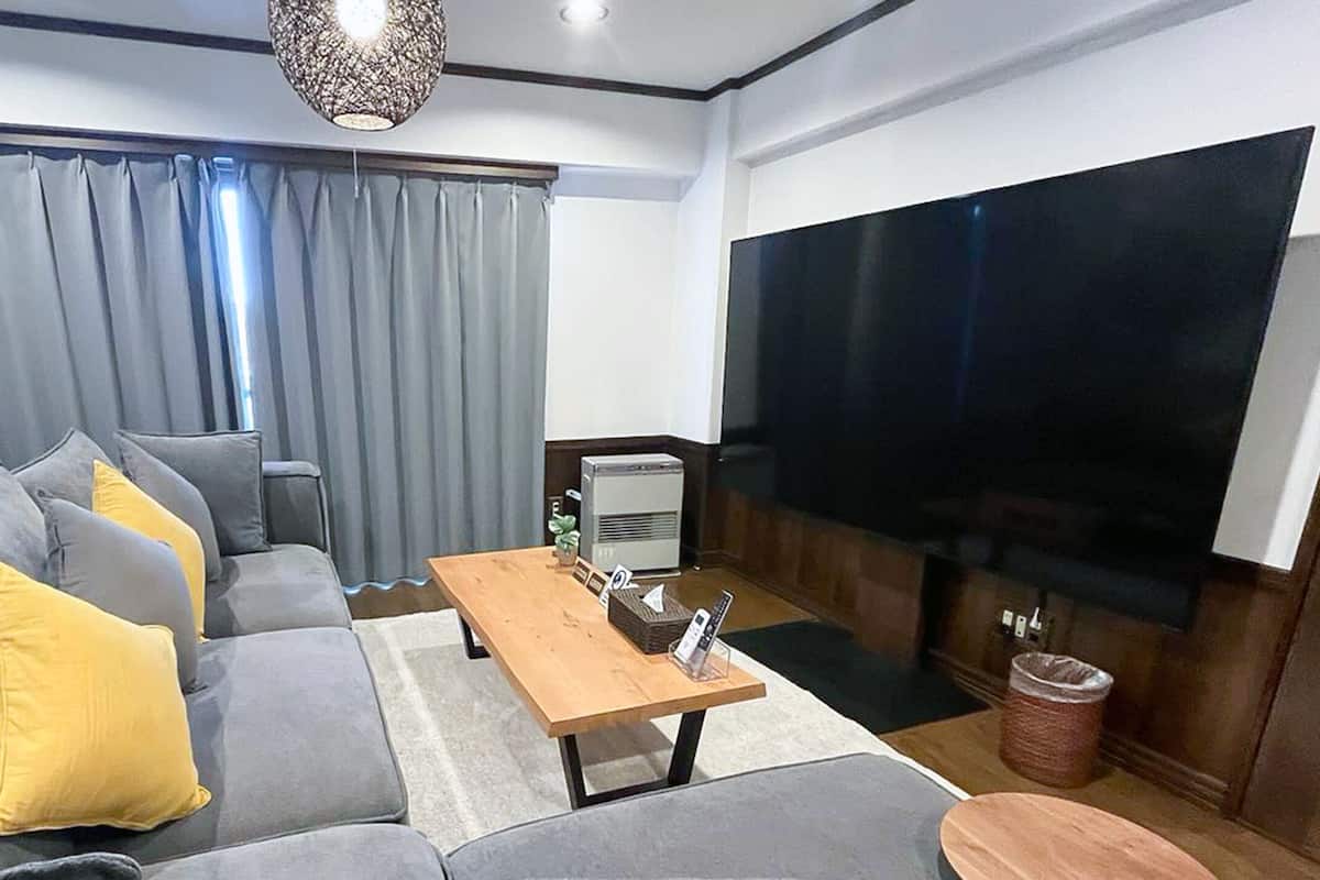 A modern living room with a grey sofa, yellow cushions, a wooden coffee table, a large flat-screen TV, and a potted plant.