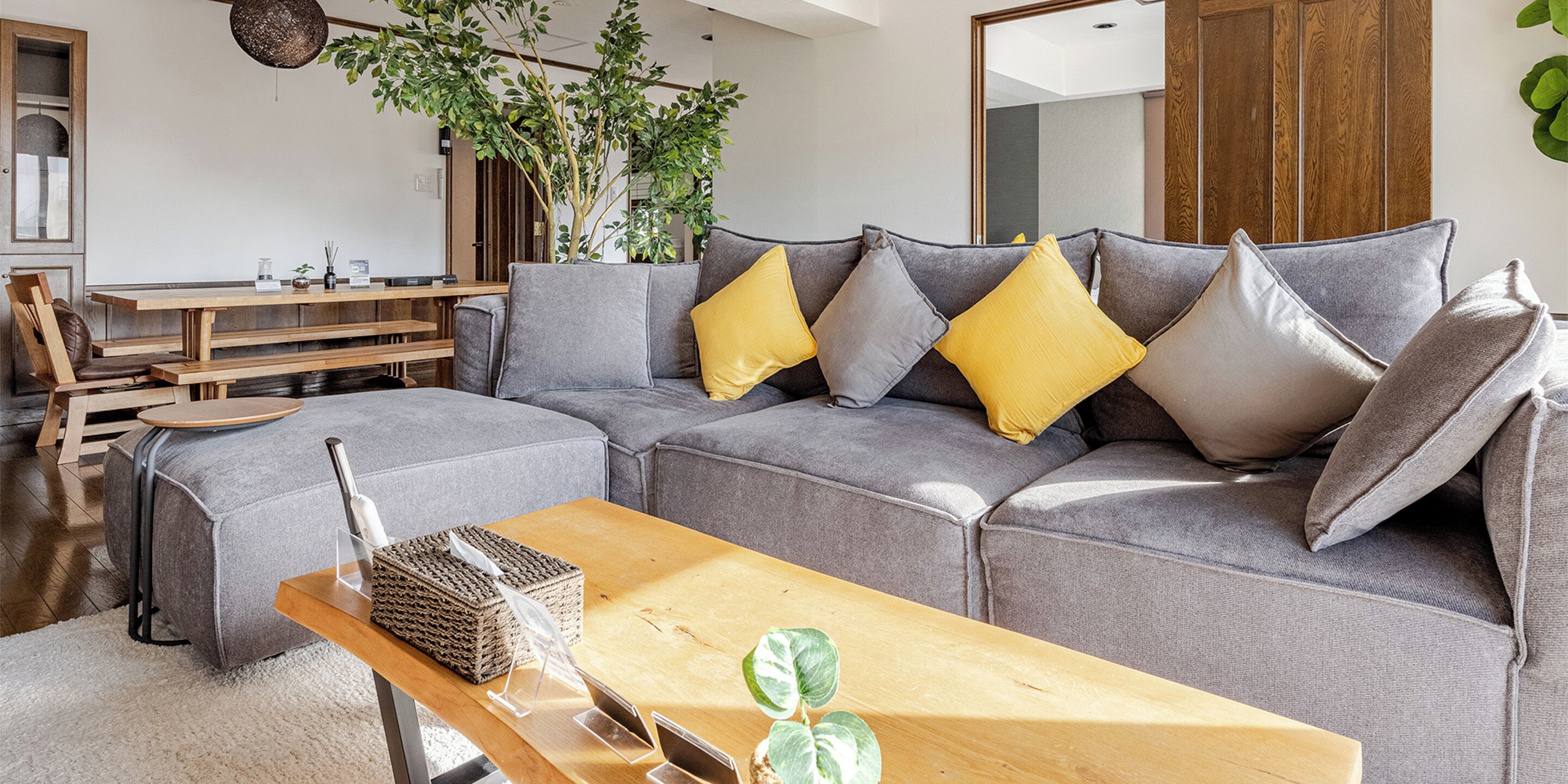 Ein modernes Wohnzimmer mit einem Ecksofa, einem Couchtisch aus Holz und einem Essbereich mit Holztisch und Stühlen.