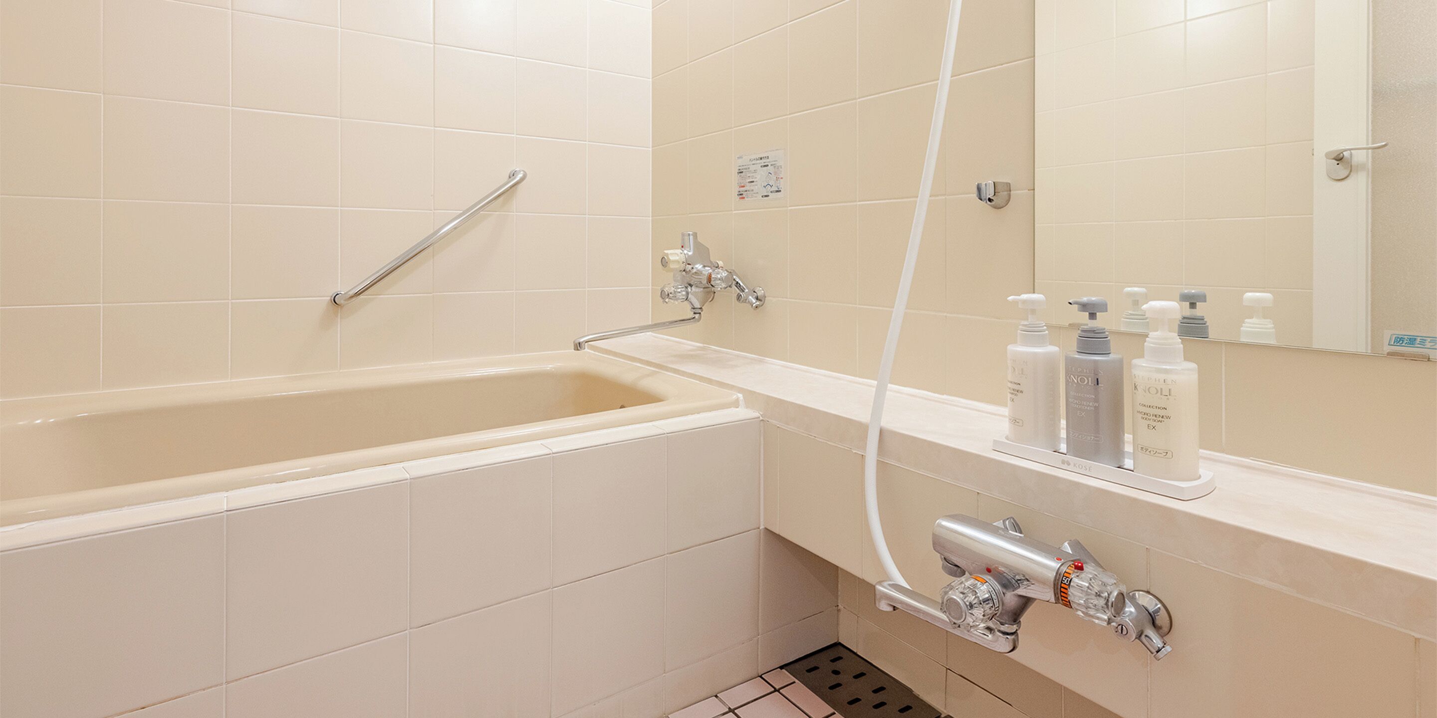 Une salle de bain moderne équipée d’une baignoire, d’une barre d’appui, d’un pommeau de douche et d’un miroir.