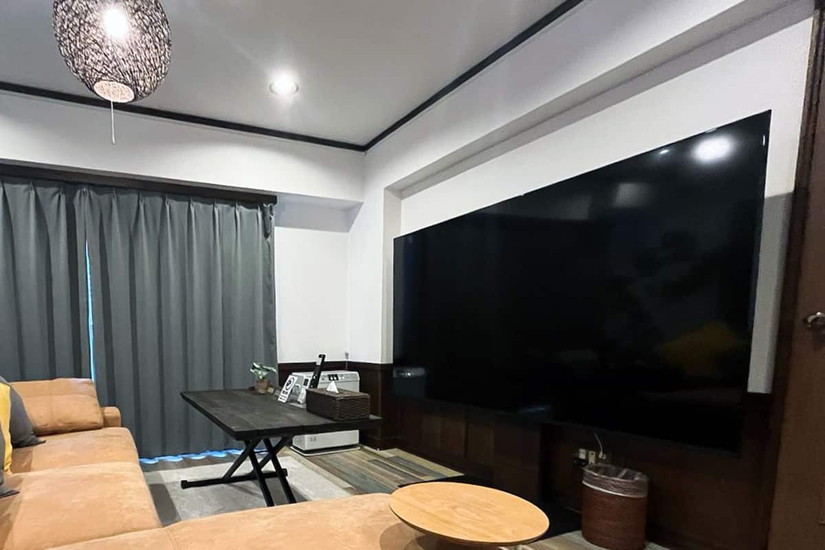 A modern living room with a large flat-screen TV, a sofa with yellow cushions, a coffee table, and a hanging light fixture.