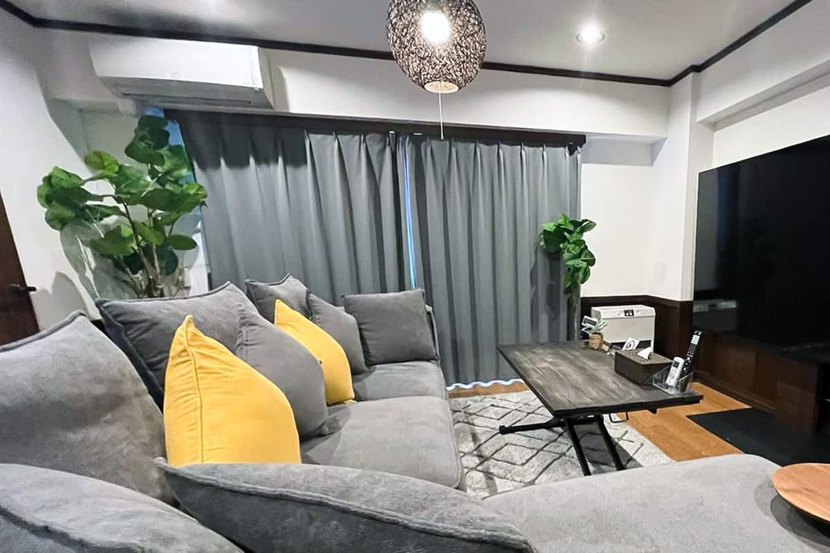A modern living room with a grey sofa, yellow cushions, a coffee table, a TV, and a plant.