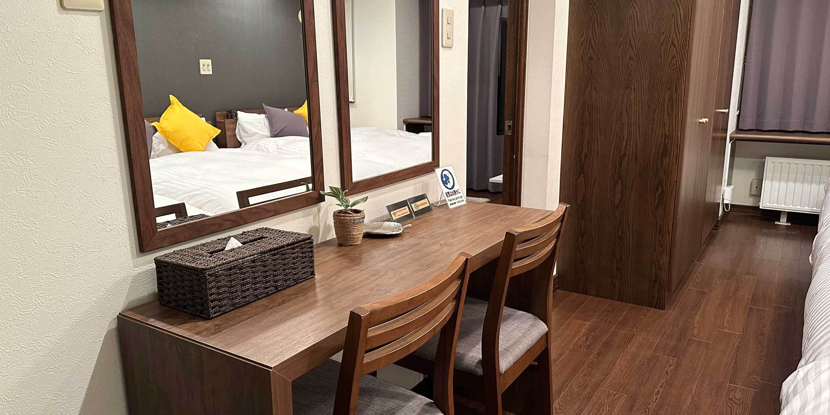 A wooden desk with a mirror, a small plant, and a sign in a hotel room.