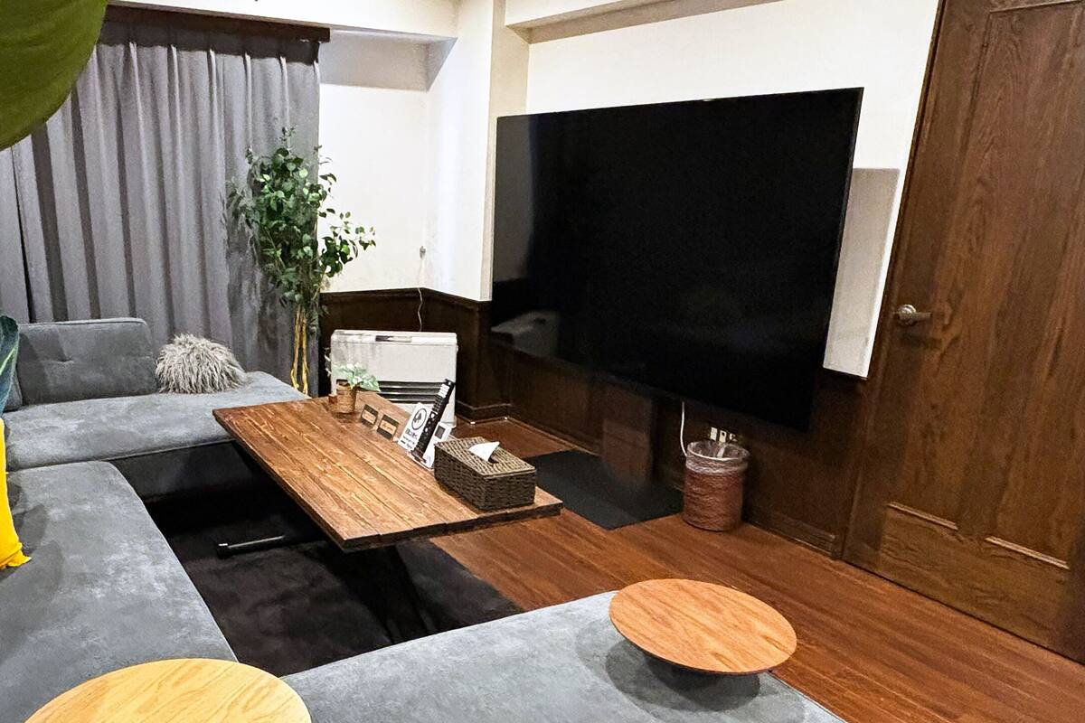 A modern living room with a grey sofa, a wooden coffee table, and a large flat-screen TV.