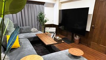 A modern living room with a grey sofa, a wooden coffee table, and a large flat-screen TV.