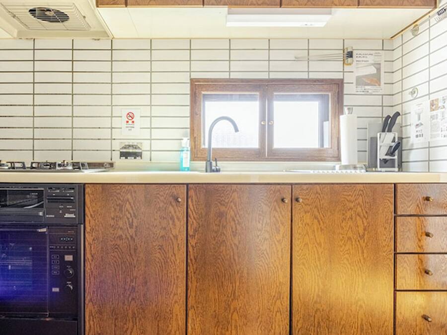 A kitchen with wooden cabinets, a built-in dishwasher, a stove, and a window above the sink.