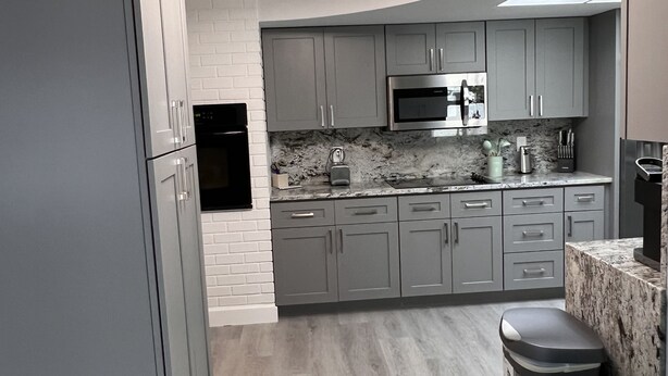 Una cocina moderna con armarios grises, un refrigerador negro, un microondas y un lavamanos.