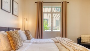 Une chambre d’hôtel avec deux lits, une fenêtre avec des rideaux, une lampe et des œuvres d’art encadrées accrochées au mur.
