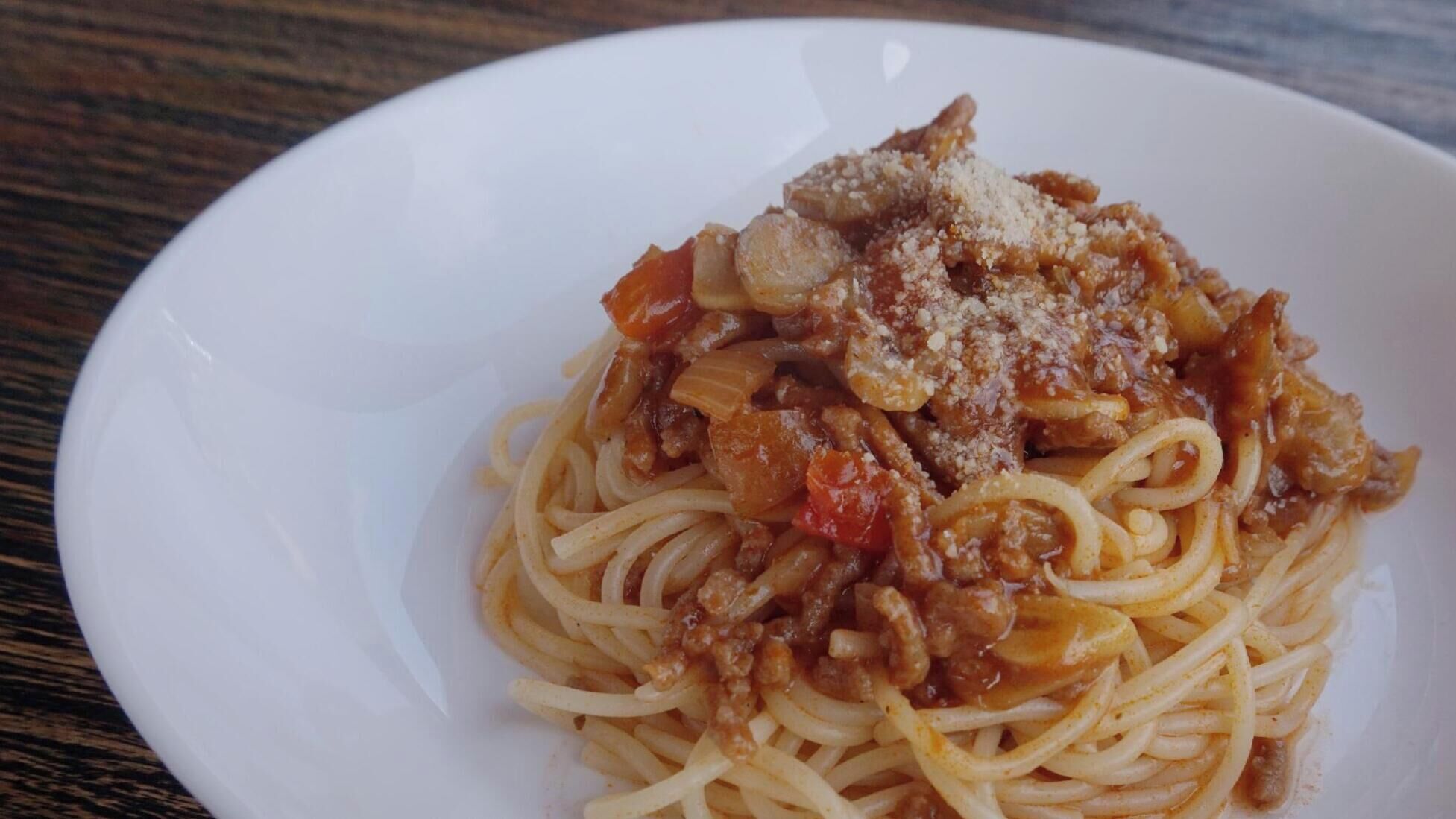 A plate of spaghetti with a meat sauce and grated cheese on a white plate.