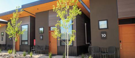 A modern building with numbered doors, outdoor seating, and small trees.