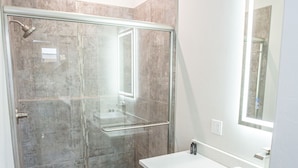 A modern bathroom with a glass-enclosed shower, a wooden vanity, and a large mirror. - The Drift (Pagosa Springs)