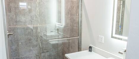 Un baño moderno con ducha de vidrio, tocador de madera y un espejo grande.